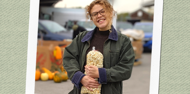 Abby Holloway holding bag of popcorn with public market in background, framed in Polaroid print with "at the market" caption