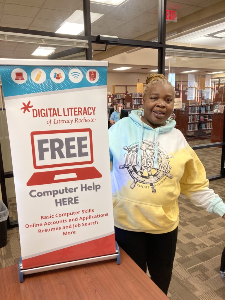Mary standing with a Digital Literacy "Free Computer Help" banner